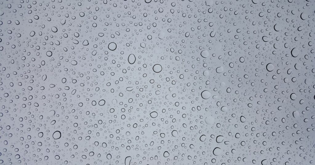 梅雨の雨粒が窓ガラスに滴る様子