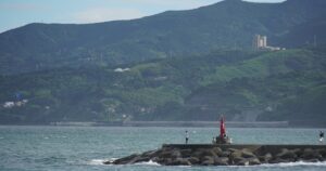 岩礁の上に立つ赤い灯台と青い海